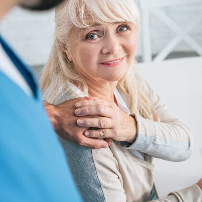 cropped shot of social worker and smiling senior woman holding hands